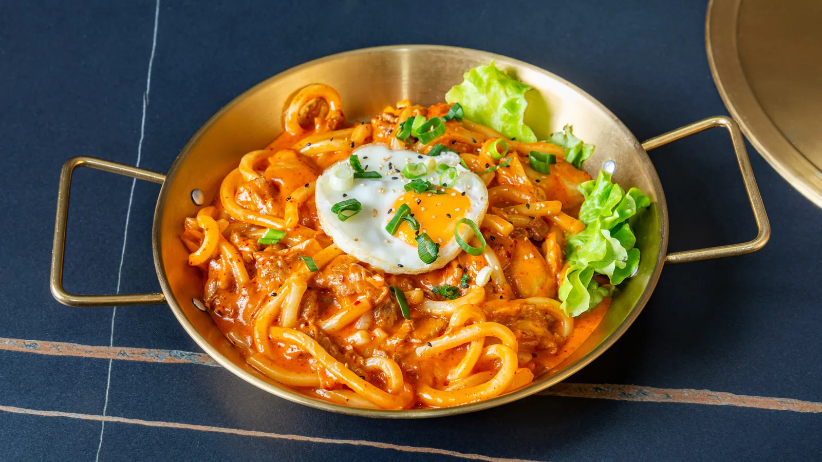 Nouilles udon en sauce rouge avec un œuf au plat, dans une poêle dorée