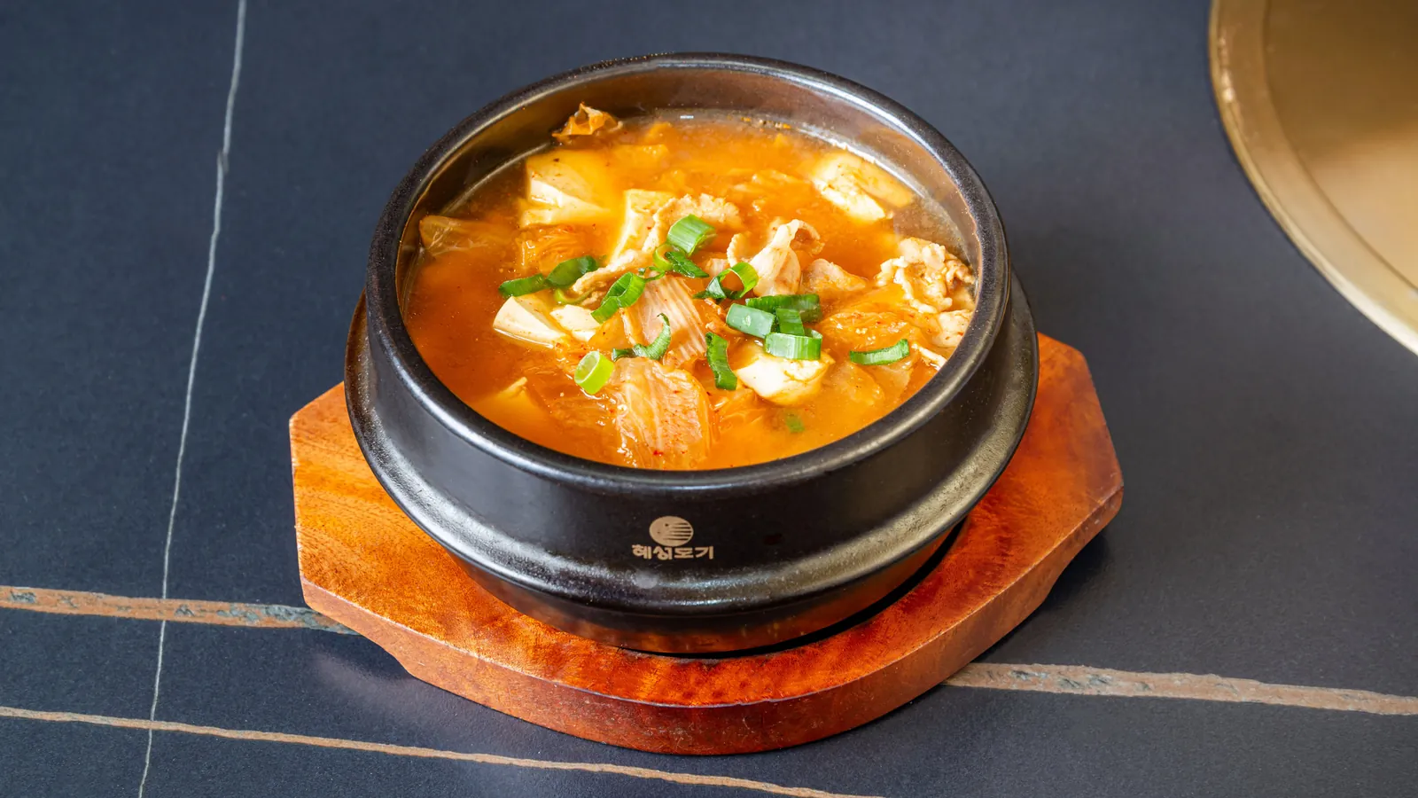 Soupe au kimchi et tofu dans un bol en fonte, sur un support en bois