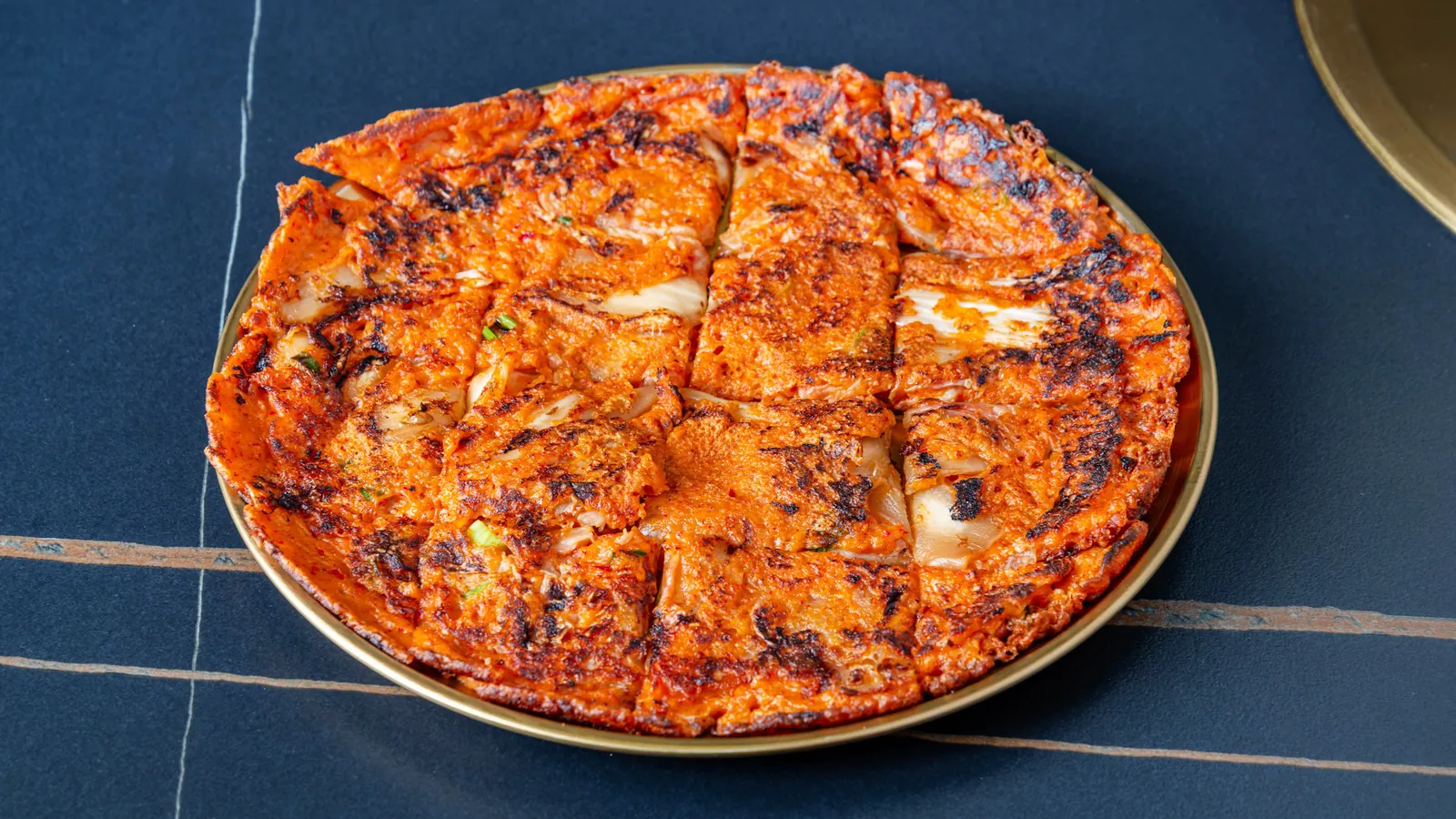 Crêpe au kimchi coupée en parts, dans un plat doré