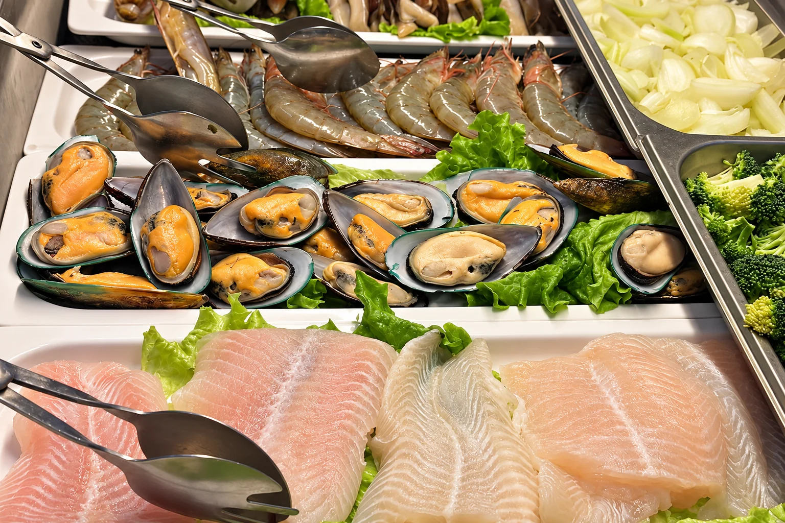 Comptoir des grillades du buffet : crevettes crues, moules en demi-coquille et filets de poisson sur feuilles de salade, oignon émincé et brocolis.