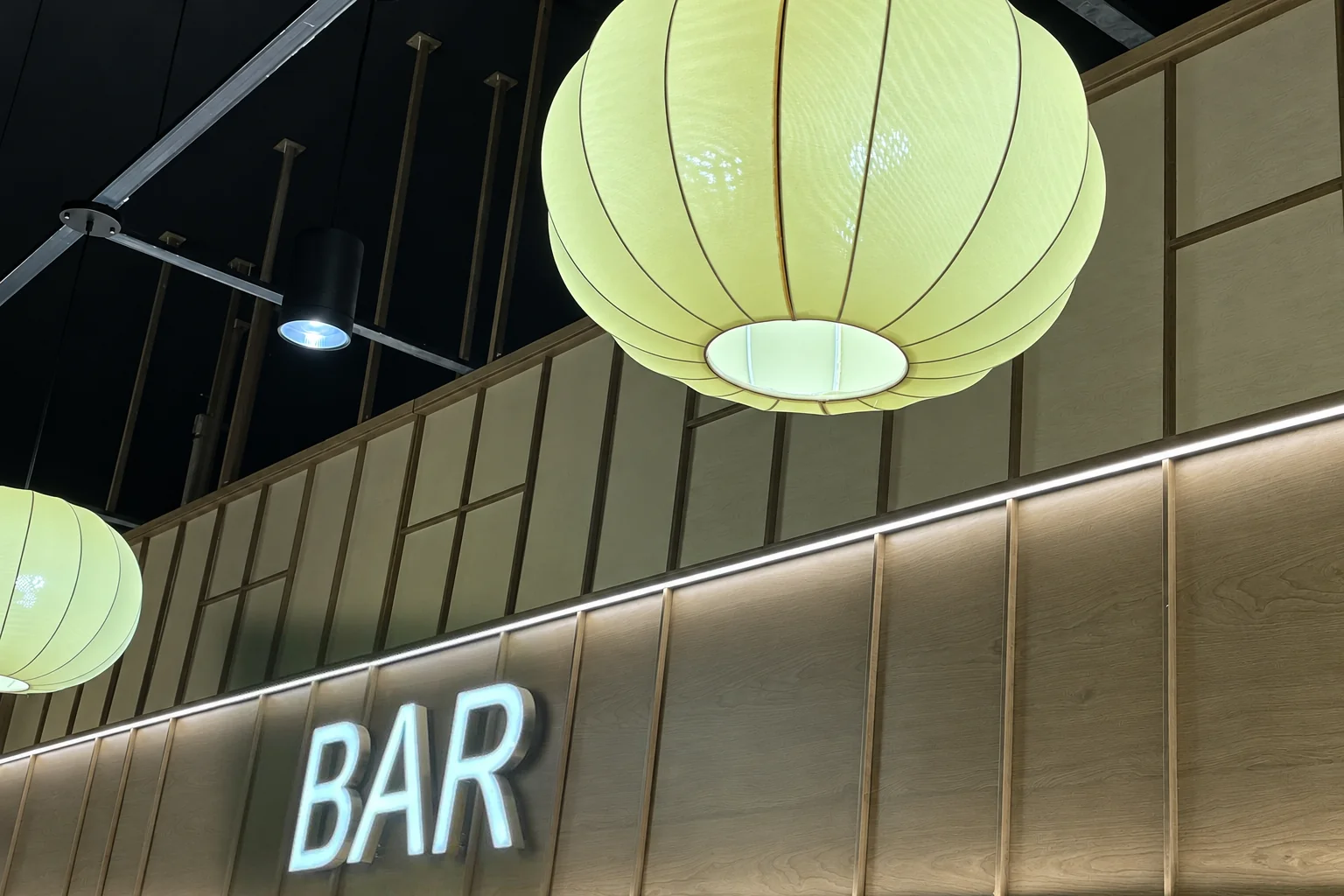 Lanterne en papier vert clair au-dessus d'un mur en bois avec l'enseigne lumineuse BAR.