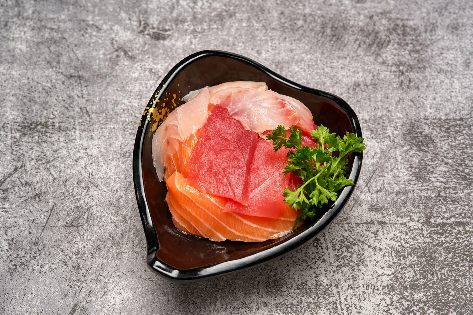 Sashimi saumon et thon avec du persil dans un bol noir en forme de cœur, fond de béton gris.